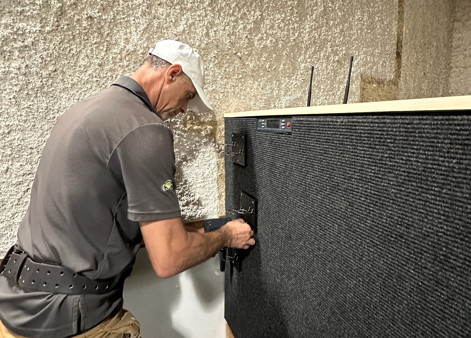 Installer attaching a mic bracket to the side of a sound booth panel during an AV setup.